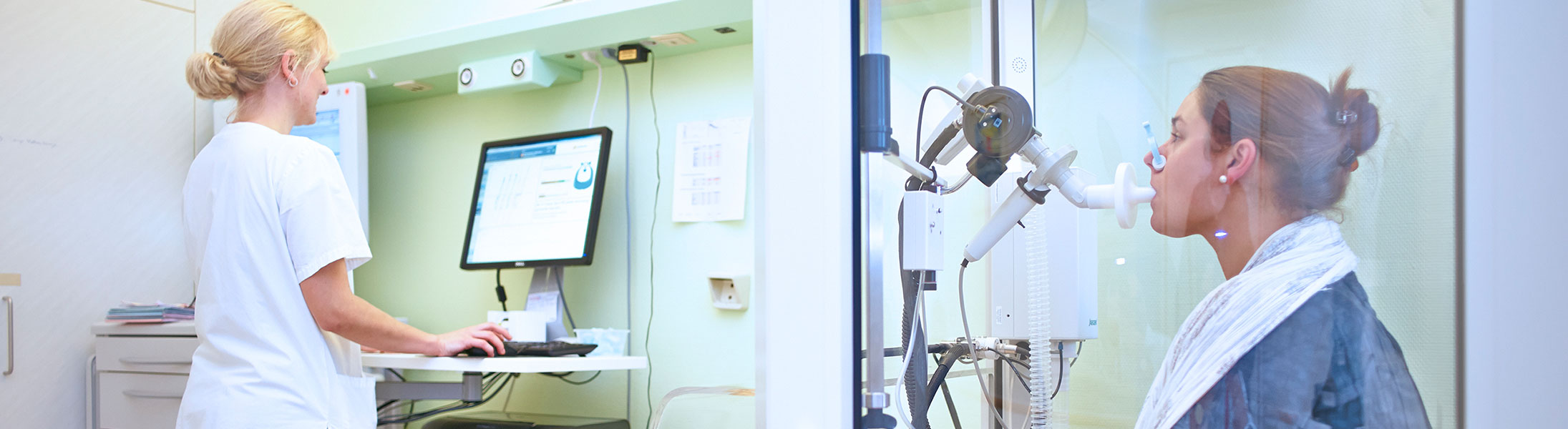 Medizinische Fachangestellte betreut eine Patientin bei einer Lungenfunktionsmessung in einer Kabine.